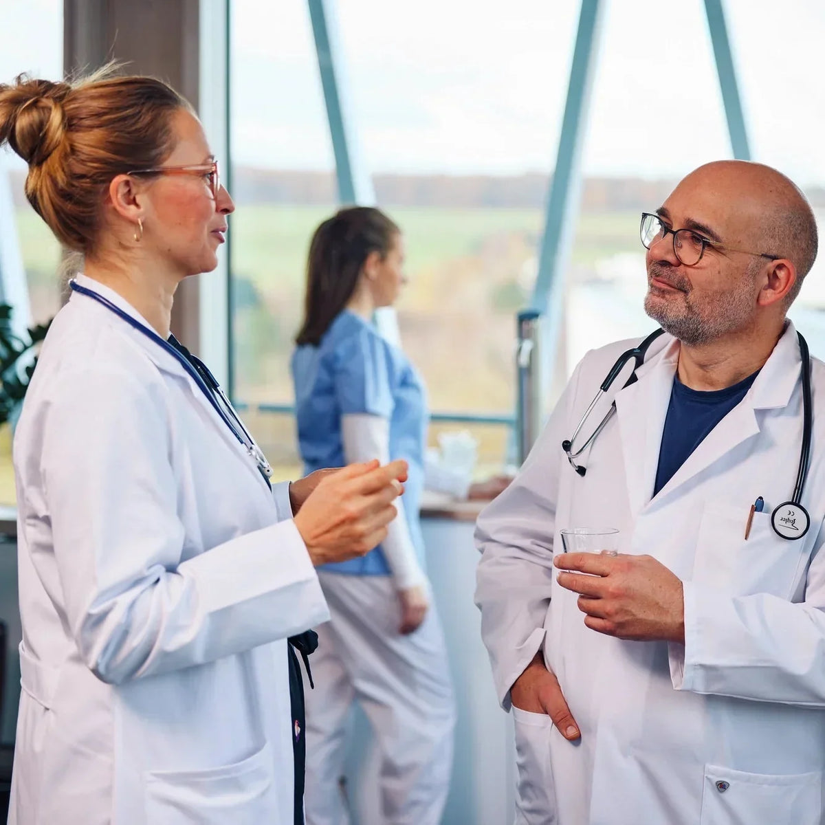 Two doctors in conversation at a hospital, with another healthcare worker in the background.