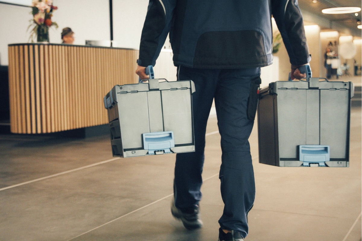 Person walking with two large toolboxes in an entrance hall.