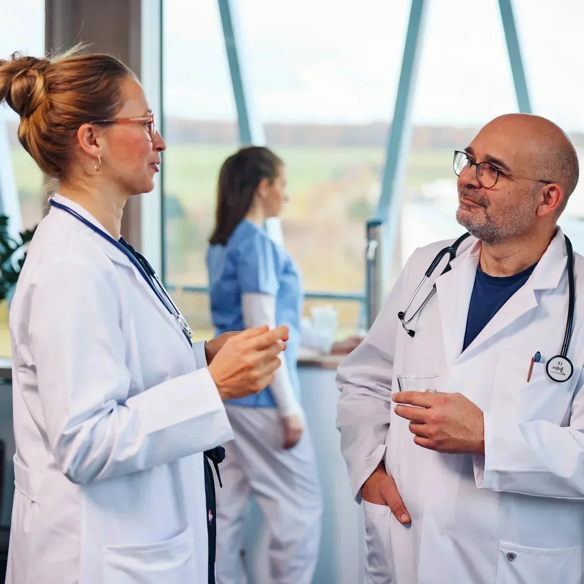Two doctors in conversation at a hospital, with another healthcare worker in the background.