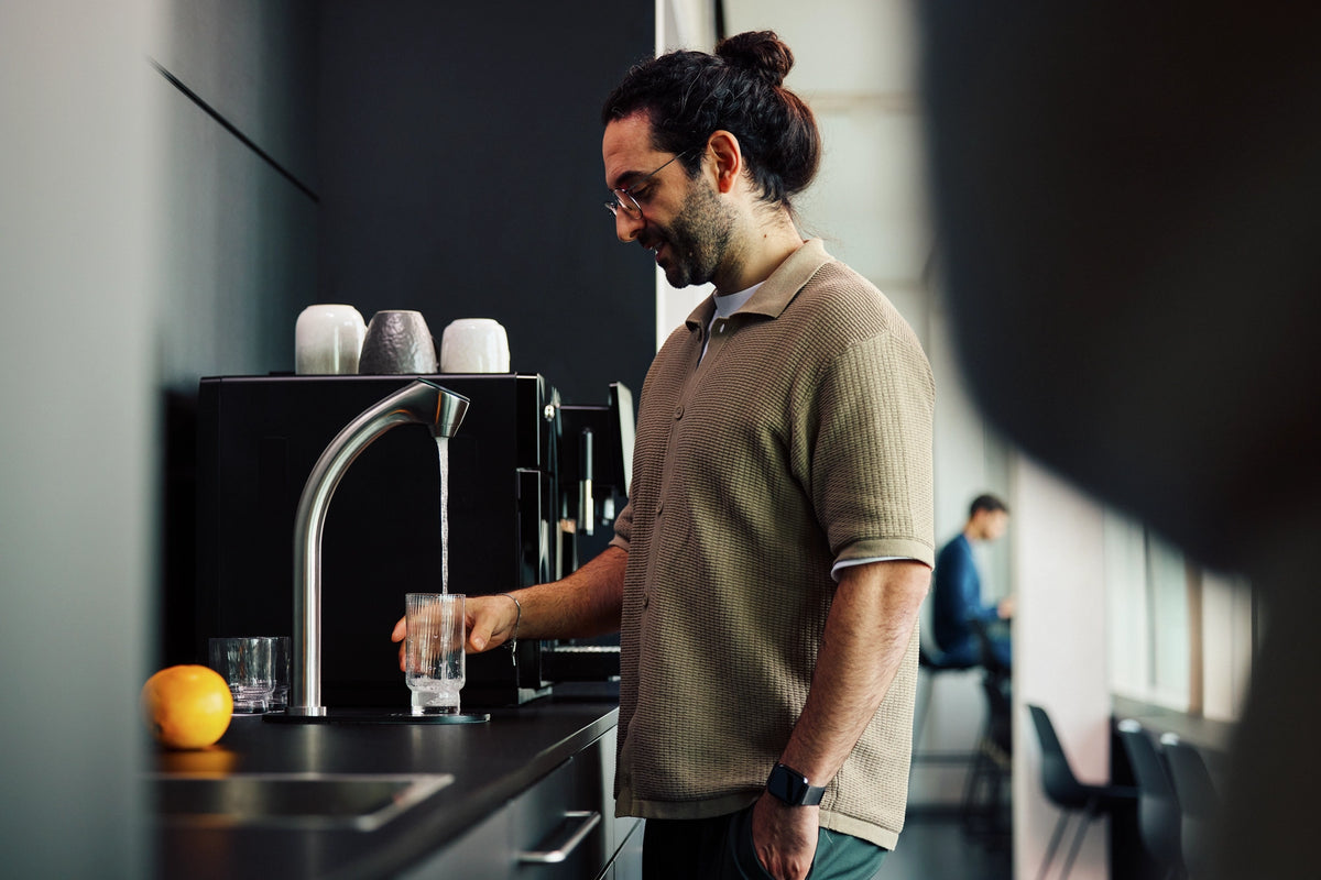 Man in a modern office kitchen dispensing water from a BRITA C-Tap