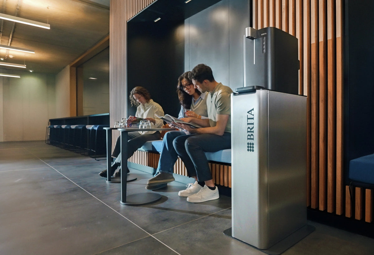 People sitting in a modern office setting with a Top Compact standing next to them.