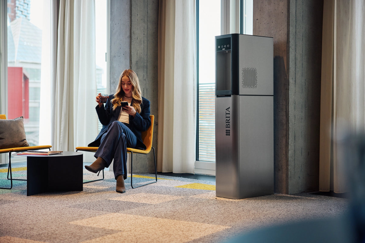 Woman sitting in a modern office space with BRITA Top Pro water dispenser.